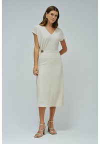 Beige midi šaty s texturou, V-výstřihem, krátkými rukávy a bočním uzlem zdobeným kulatým zlatým knoflíkem. Kombinované s páskovými podpatky.