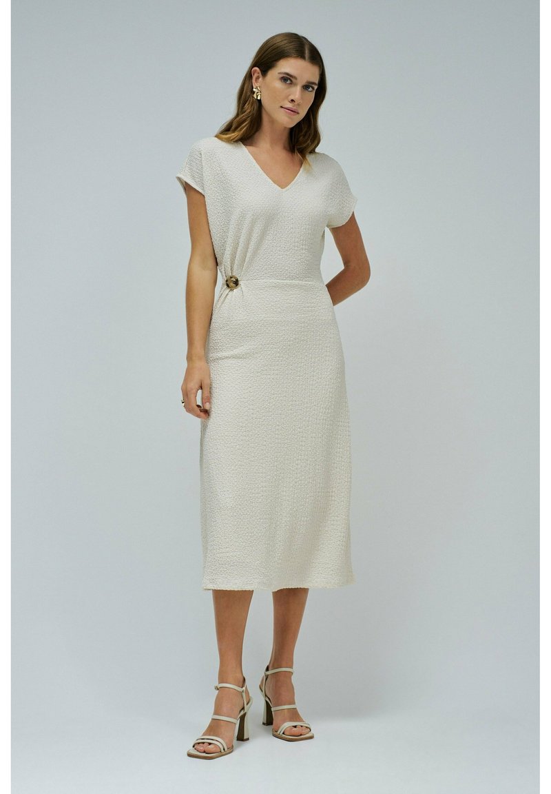 Beige midi šaty s texturou, V-výstřihem, krátkými rukávy a bočním uzlem zdobeným kulatým zlatým knoflíkem. Kombinované s páskovými podpatky.