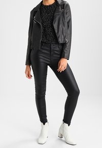 Giubbotto di pelle nero, top a pois neri, pantaloni skinny neri e stivaletti bianchi alla caviglia. I dettagli notevoli includono zip e design aderente.