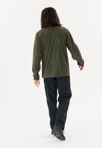 Camisa de manga larga estilo forro polar en color verde oliva, combinada con pantalones y botas negras. La camisa tiene un corte holgado y una textura suave.