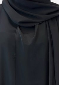 Zwarte, lichte stof hangt met een gladde textuur. Heeft een geraffineerde halslijn en een vloeiende sjaalachtige sectie aan één kant.