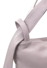 Lyse lilla læderhåndtaske med en struktureret overflade. Inkluderer en bred, flad skulderrem med en unik drejning.