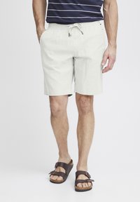 Lys grå shorts med elastisk midje og snøring, med side-lommer og en avslappet passform, kombinert med mørkebrune sandaler.