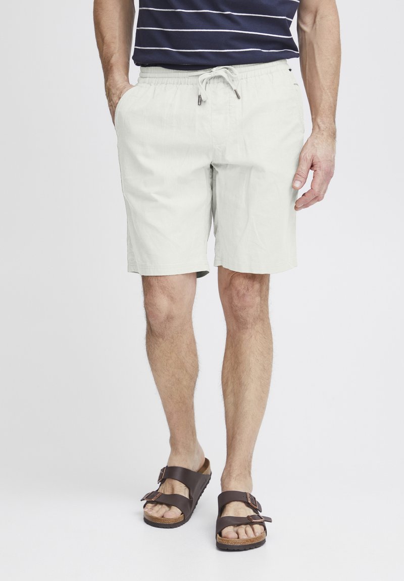 Lys grå shorts med elastisk midje og snøring, med side-lommer og en avslappet passform, kombinert med mørkebrune sandaler.