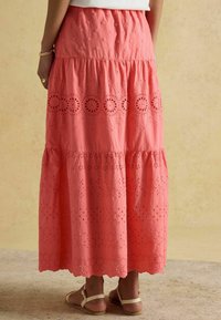 Fustă maxi coral cu straturi suprapuse, broderie cu ochiuri, tiv ondulat și material texturat. Asortată cu sandale plate.