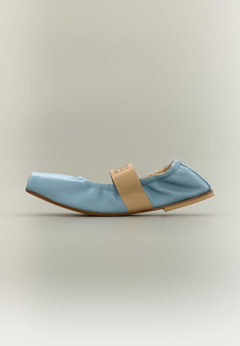 Φλατ παπούτσι από ανοιχτό μπλε δέρμα με τετράγωνη μύτη, μπεζ ελαστικό λουράκι στο επάνω μέρος και μαλακή σόλα σε ουδέτερο φόντο.