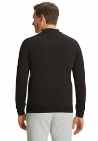 Maglione nero a maniche lunghe in maglia liscia con scollo rotondo e polsini a coste, abbinato a pantaloni grigio chiaro.