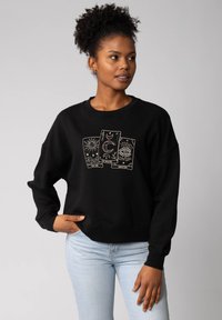 Zwarte sweatshirt met drie tarotkaartontwerpen in goud: "De Zon," "De Maan," en "Bestemming." Relaxte pasvorm, zachte textuur, geribde manchetten.