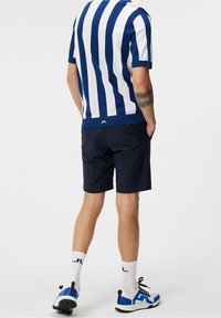 Modrá a bílá pruhovaná polo tričko s krátkým rukávem, námořnické šortky, sportovní boty s modrými akcenty a bílé ponožky. Neformální sportovní vzhled.