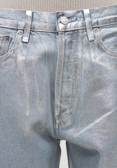 Ανοιχτό μπλε τζιν με μεταλλική όψη, μπροστινές τσέπες, θηλιές για ζώνη και κλειστή κουμπότρυπα σε φόντο ριμπ μπεζ τοπ.