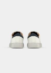 White sneakers with a textured rubber sole, leather upper, and contrasting navy and tan accents on the heel tab. Minimalist design.