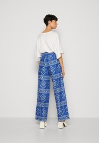 Pantalons larges avec un motif tribal bleu, associés à un top oversize blanc. Les pantalons sont ornés de motifs géométriques et d'accents.