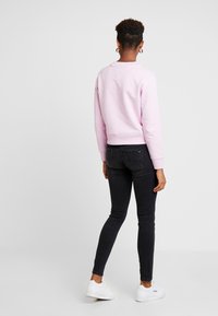 Sudadera de color rosa claro con puños y dobladillo acanalados, combinada con jeans skinny negros y zapatillas blancas, vista desde atrás.
