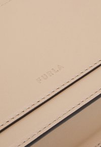 Bolso de mano de cuero beige con el logotipo "FURLA" en relieve, costuras cuidadas y una textura suave en un diseño estructurado.