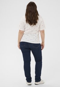 Weißes T-Shirt mit kleinen roten Herzmustern, kurze Ärmel, kombiniert mit dunkelblauen Skinny-Jeans und weißen Sneakers. Schlichtes Design, lässige Passform.