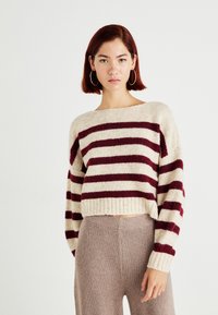 Geknipte gebreide trui met brede rode en crèmekleurige strepen. Heeft een bootnek en geribbelde manchetten. Gepaard met beige, gestructureerde, hooggewaist broek.
