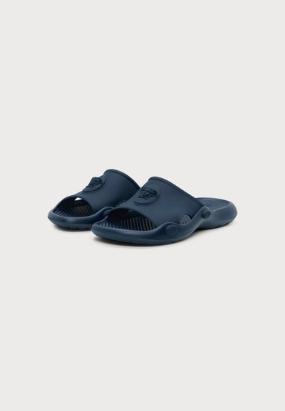 Paire de sandales bleu marine à bout ouvert, faciles à enfiler, avec des semelles intérieures texturées et un emblème en relief sur les brides avant, sur un fond clair uni.