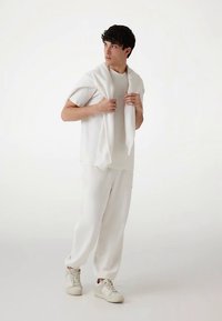 Biały bawełniany strój składający się z krótkiego topu z krótkim rękawem i spodni z troczkiem. Miękki, ubrany w podobnym odcieniu sweter luźno narzucony na ramiona.