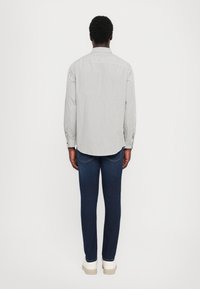 Hvitt langermet skjorte med svarte prikkene, kombinert med mørkeblå jeans og lyse sneakers, sett fra baksiden.