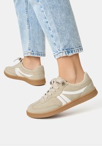 Sneakers beige con dettagli bianchi e lacci. Materiali in morbido camoscio e pelle liscia, punta rotonda e suola in gomma. jeans tagliati sopra la caviglia.
