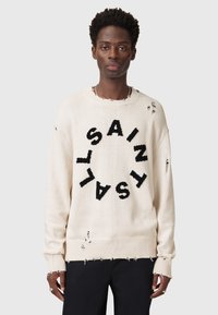 Helles beiges Sweatshirt mit großem schwarzen "SAINT"-Text in einem kreisförmigen Design, das abgenutzte Details sowie gerippte Bündchen und Saum aufweist.
