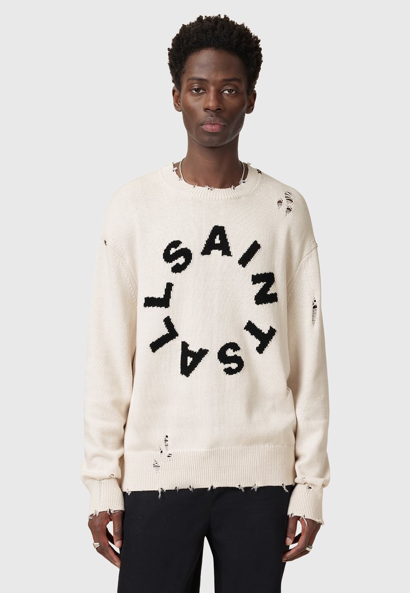 Helles beiges Sweatshirt mit großem schwarzen "SAINT"-Text in einem kreisförmigen Design, das abgenutzte Details sowie gerippte Bündchen und Saum aufweist.