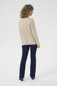 Beige stickad tröja med långa ärmar, detalj med ryggspringa, i kombination med mörkblå utsvängda jeans och svarta klackskor.