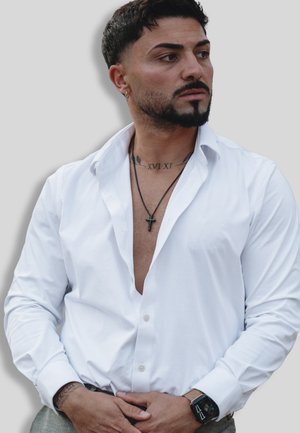 Weißes Hemd mit offenem Kragen, langärmlig und mit glatter Textur. Schwarze Kreuzkette und Smartwatch als Accessoires.