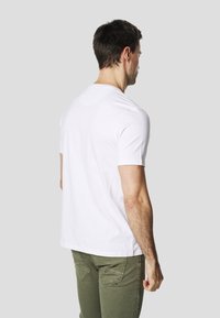 T-shirt en coton blanc à manches courtes, col rond, et design uni, associé à un pantalon vert olive avec des coutures décoratives.