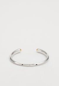 Pulsera de brazalete de plata con extremos afilados. Los extremos cuentan con acentos redondos de oro, textura suave y un diseño minimalista. Sin patrones visibles.
