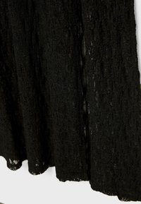Schwarzes Spitzenkleid mit einem strukturierten Muster und einer fließenden Silhouette. Der Stoff wirkt leicht und leicht transparent.