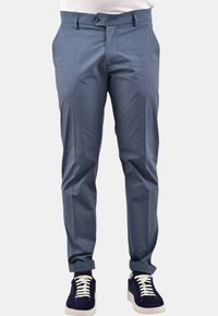 Pantaloni slim-fit azzurro chiaro con chiusura frontale a bottone e due tasche laterali, abbinati a sneakers scure con lacci bianchi.