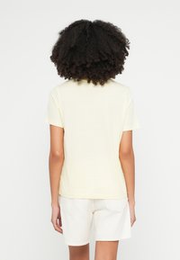 Hellgelbes Baumwoll-T-Shirt mit kurzen Ärmeln und rundem Ausschnitt, kombiniert mit weißen Shorts. Einfaches, lässiges Design ohne Muster.