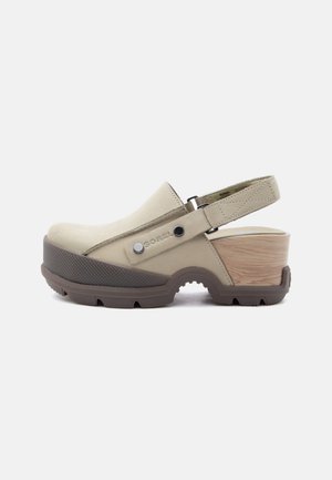 Bézs zárt orrú klumpa állítható boka pánttal, vastag barna mintázott talppal és fa textúrájú blokksarokkal.