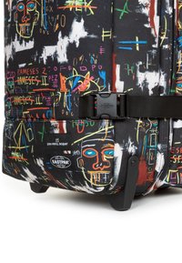 Rullväska med svart tyg som har färgglad graffiti-liknande konst, säkrad med en svart spänne och utrustad med robusta hjul.