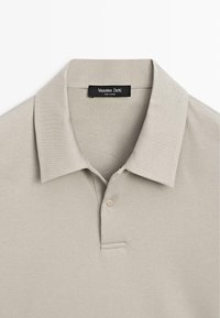 Lichtgrijs poloshirt gemaakt van zachte stof. Heeft een klassieke kraag, een tweeknopsbies en discreet stiksel op de bies.