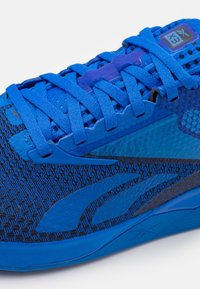 Blå sportskor med ett strukturerat nätövre, förstärkt snörningssystem och en slät gummisula med kontrasterande mörkblå detaljer.
