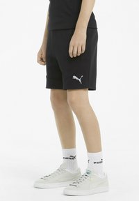 Czarne sportowe szorty z bocznymi szwami, logo Puma w białym kolorze, zestawione z jasnoszarymi trampkami i białymi skarpetkami z czarnym logo.