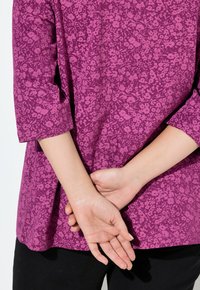 Haut à motifs floraux violets avec des manches trois quarts, vu de dos. Tissu lisse aux couleurs vives et coupe décontractée.