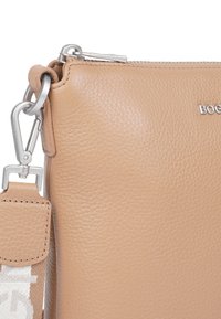 Läderhandväska i beige med en texturerad yta. Har en silvrig dragkedja och en avtagbar rem med ett vävt mönster.