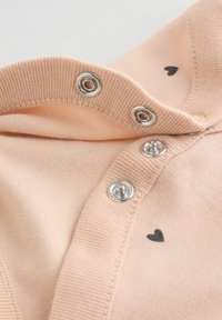 Puha rózsaszín anyag ezüst patentokkal és apró fekete szívmintákkal a ruhanyílás szélén.