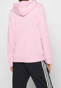 Jasnoróżowy hoodie z kieszenią kangurką i ryflowanymi mankietami. Posiada sznurki do ściągania przy kapturze oraz gładką tkaninę z mieszanki bawełny. W zestawie z czarnymi spodniami.