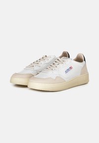 Sneaker bianche in pelle con dettagli in suede beige, punta forata, lacci piatti e suola in gomma testurizzata. Presentano un'etichetta con logo sul lato.