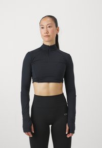 Svart, cropped langermet topp med høy krage og delvis glidelås, med tettsittende ermer som har tommelhull. Smooth, elastisk stoff.