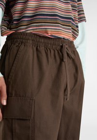 Brązowe spodnie cargo na elastycznej talii z bocznymi kieszeniami, wykonane z teksturowanej tkaniny, w luźnym kroju, połączone z topem w wielokolorowe paski.