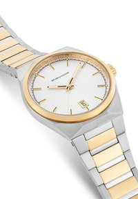 Reloj de acero inoxidable con un dial texturizado en plata, acentos en oro y una ventana de fecha. La pulsera combina eslabones de plata y oro.