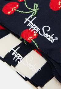 Marineblaues Sockenpaar mit roten Kirschmustern und grünen Stängeln, darauf steht in weißem Text "Happy Socks". Der Hintergrund zeigt gestreifte Designs in Creme und Marineblau.
