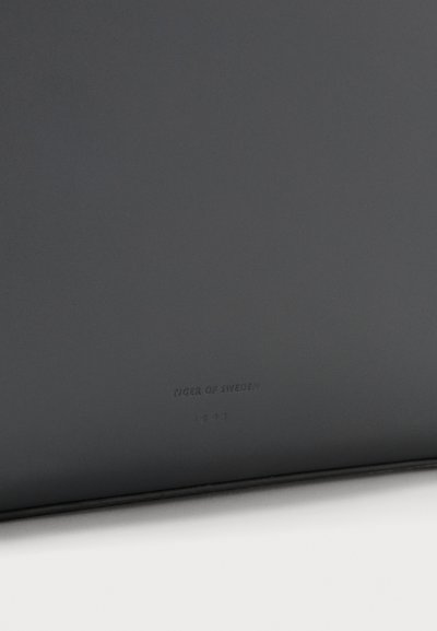 Αξεσουάρ από μαύρο δέρμα με λεία υφή, με ανάγλυφο το λογότυπο "TIGER OF SWEDEN 1903" στο κάτω μέρος, απλός ορθογώνιος σχεδιασμός.