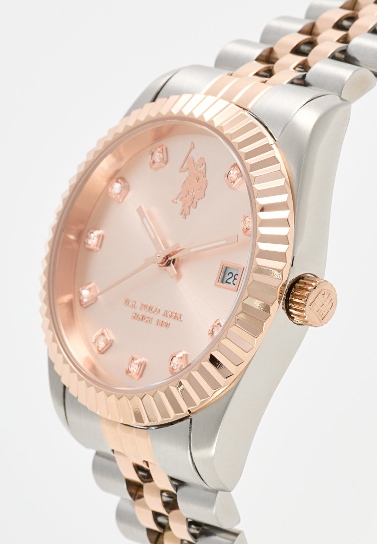 Montre-bracelet en argent et or rose avec une lunette cannelée, un cadran rose, des index en cristal, et un bracelet en métal avec des couleurs alternées.