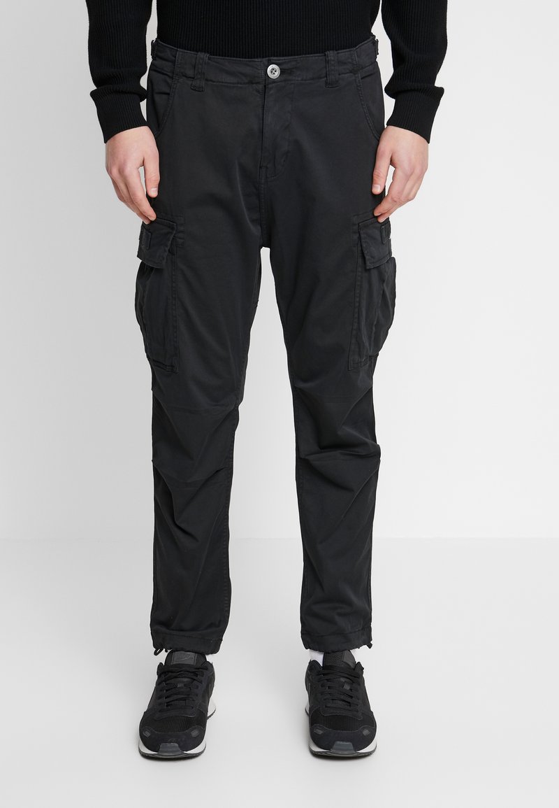 Sorte cargo bukser lavet af letvægtsstof med flere sidelommer, knaplukning og tapered ankler. Båret med sorte sneakers.